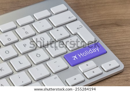 Holiday and aircraft symbol on a large blue button of a modern keyboard on a wooden desktop