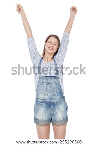 Happy young fashion girl in jeans overalls with hands up isolated on white background