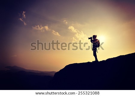 young woman photographer taking photo on sunset mountain peak