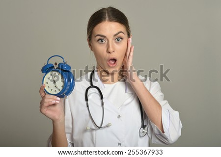 Female doctor with clock, standing on grey background