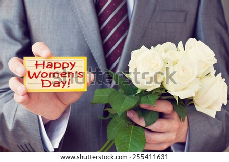 Happy Women's Day! Man wearing a suit holding a greeting card and white roses