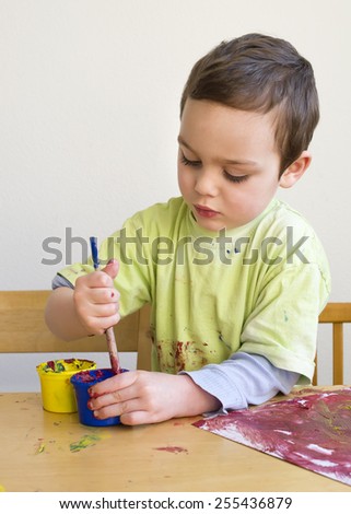 Child boy painting a picture with brush at home or school nursery.
