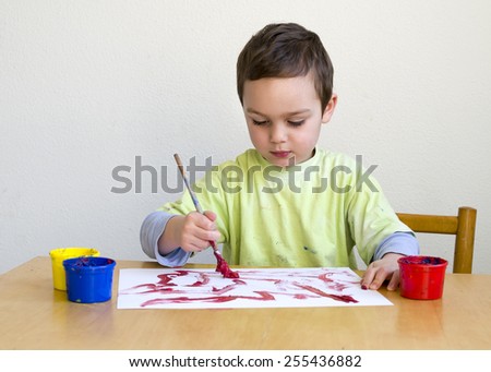 Child boy painting a picture with brush at home or school nursery.