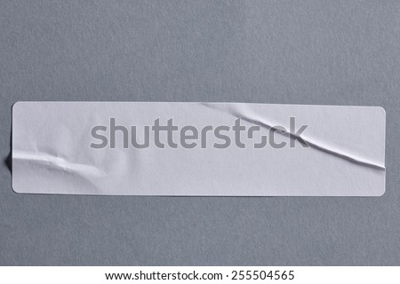 White Adhesive Paper Tag on Grey Cardboard Background with Real Shadow. Sticker Label Close Up. Top View with Copy Space for Text or Image