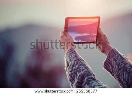 Young woman taking pictures on a tablet in mountains at sunset. Toned picture