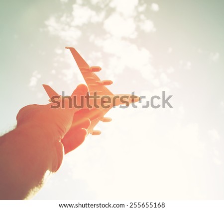 close up photo of man's hand holding toy airplane against blue sky with clouds
