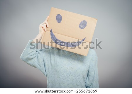 Young girl holding a cardboard with a smiley face on it in front of his head
