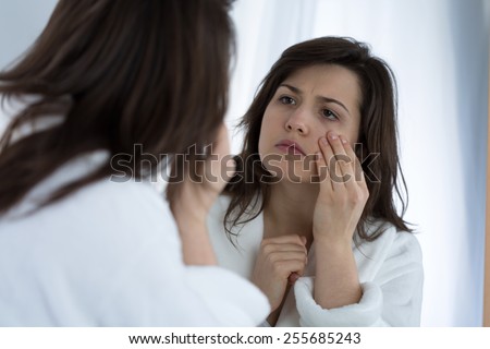 Young sad woman looking in the mirror at her wrinkles Royalty-Free Stock Photo #255685243