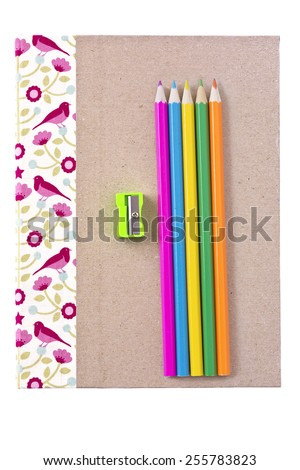 A notebook with color pencils and pencil sharpener on top of a white background