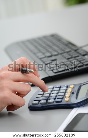close up detail of hands typing on calculator with a desktop computer keyboard