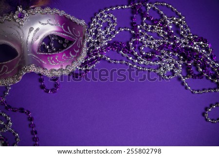 A purple mardi gras mask on a purple background with beads.  Carnivale costume.