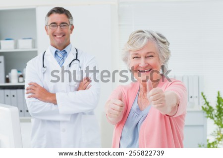 Portrait of happy female patient showing thumbs up sign while standing with doctor in clinic