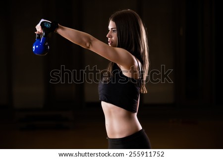 Low key fitness woman working out with kettle bell.Young adult fitness woman doing exercises with a kettle bell as a part of a fitness workout.Kettle bell workout