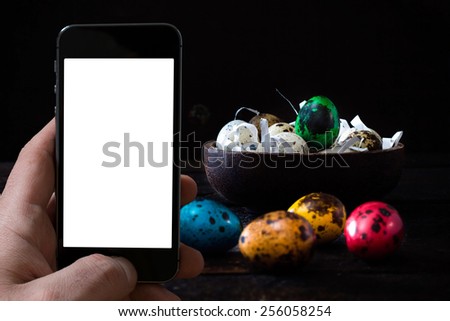 Selective focus on the green Easter egg in wooden bowl.Blank screen of mobile phone