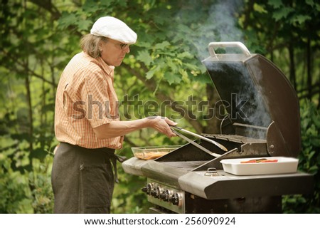 Senior man grilling outdoors. Smoke rises from the barbecue. The picture is desaturated and has been treated with digital filters
