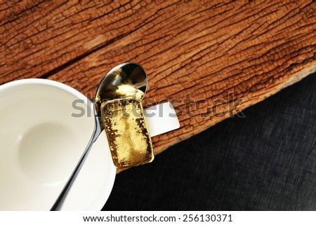 Gold bar put on the coffee cup in the scene appear coffee spoon also. The hard wood brown color and black color leather is a background represent the business and investment concept idea.
