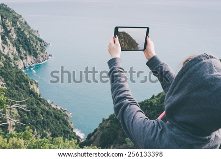 Young woman taking pictures on a tablet in mountains. Toned picture