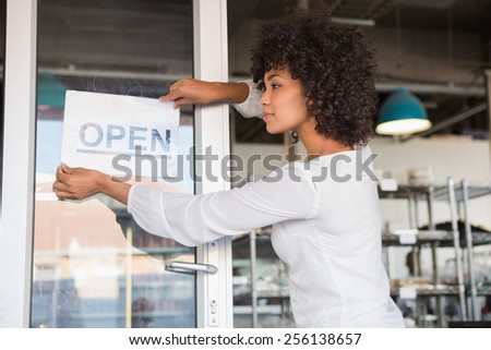 Pretty worker putting up a open sign at the bakery