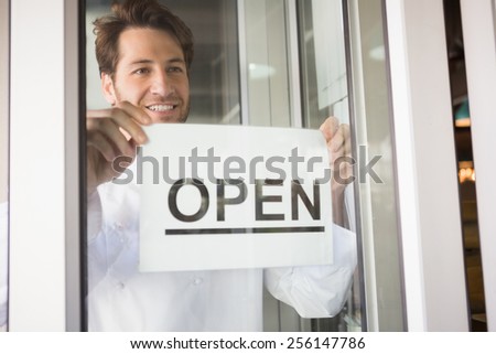 Smiling chef putting up a sign on windowat the bakery