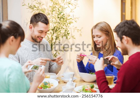 people, leisure, friendship and technology concept - group of happy friends with smartphones taking picture of food at cafe