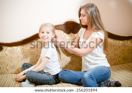 Picture of young pretty woman making hairstyle her girl child on sofa