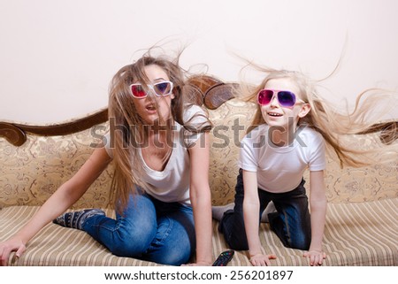 Young beautiful woman with blond little girl sitting in 3D glasses on sofa