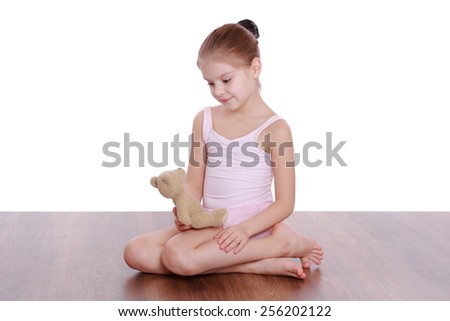 Beautiful little girl holding a teddy bear and is engaged in gymnastics on a wooden floor on a white background