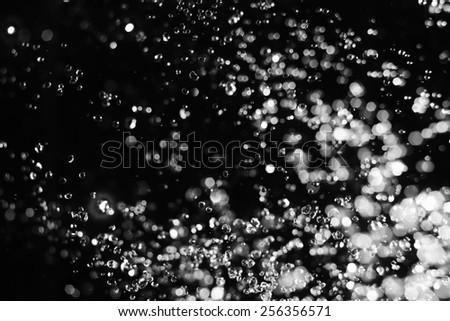 Water drops and blurred spot of light levitating in the air on black background
