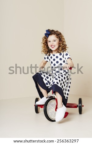 Young girl in spotty dress riding tricycle