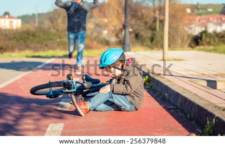 Boy in the street ground with a knee injury screaming after falling off to his bicycle Royalty-Free Stock Photo #256379848