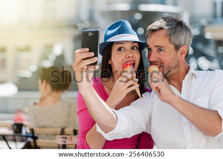 Portrait of a smiling couple eating ice cream and having fun in the city. The grey hair man with a beard is taking a selfie with phone. they make funny faces