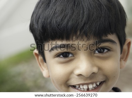 A south asian, indian origin boy with a natural smile looking at camera in out doors with blurred background.