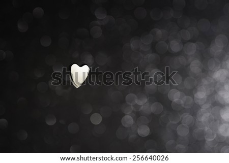 A black and white photograph of a heart made of metal in a blurred dark background with unfocused light