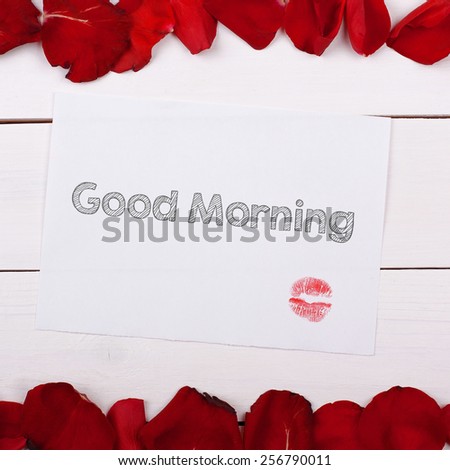 Sheet of paper Good Morning with a kiss. Note and rose petals on the table