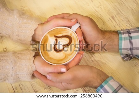 Four hands wrapped around a cup of coffee with heart drawing