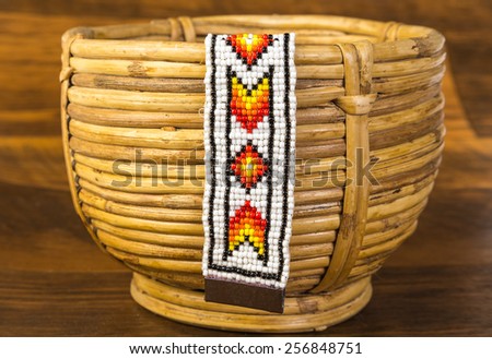 Colorful Native American beaded bracelet hanging from vintage spiral woven wicker basket against rustic wood background.