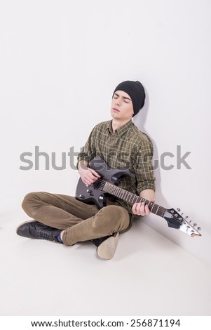 Young male musician is playing a six-string bass guitar is sitting on the floor, in studio.