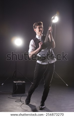 Young guitarist with the electric guitar, isolated on dark background.