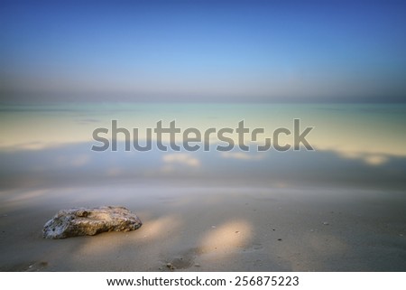 A rock on a white sand beach and blue ocean on horizon. Long exposure photography.
