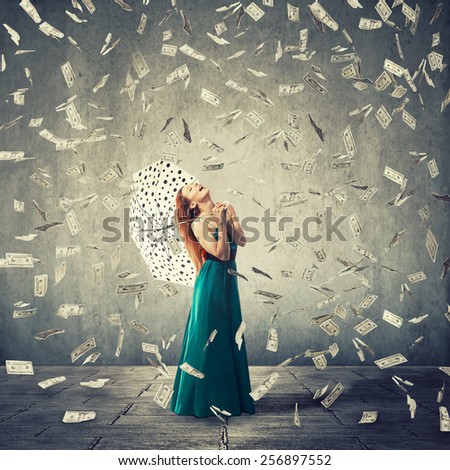 Excited young woman with umbrella under a money rain isolated on grey wall background. Positive emotions financial success luck good economy concept 