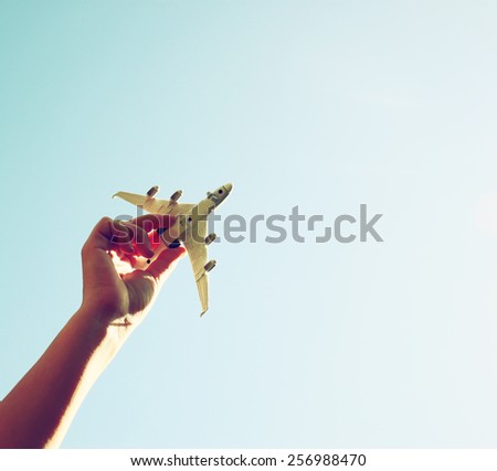 close up photo of woman's hand holding toy airplane against blue sky . image is retro filtered 