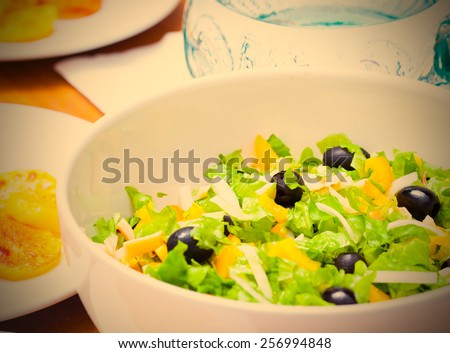 Assorted salad of green leaf lettuce with squid and black olives on lunch table, close up. instagram image retro style