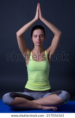 young woman sitting in lotus position over grey background