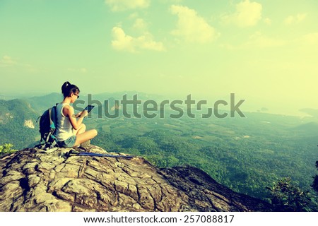 woman hiker use digital tablet at mountain peak cliff