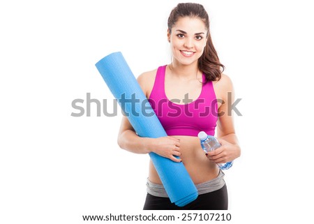 Attractive young woman with a yoga mat and a bottle of water in a white background with some copy space