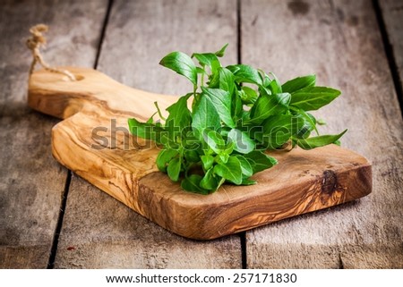 bunch of fresh organic basil in olive cutting board on rustic wooden background Royalty-Free Stock Photo #257171830