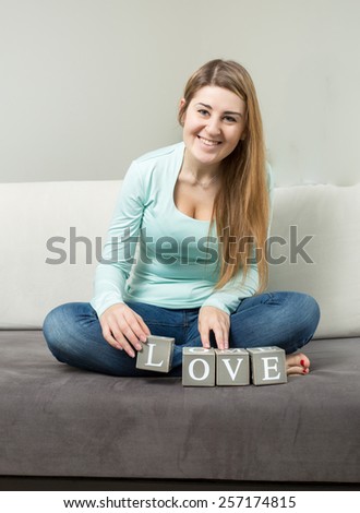 Cute young woman making word "love" from bricks on sofa
