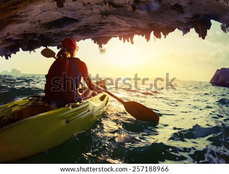 Young lady paddling the kayak from limestone cave towards open sea Royalty-Free Stock Photo #257188966