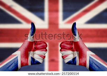 United Kingdom flag painted on female hands thumbs up with blurry wooden background