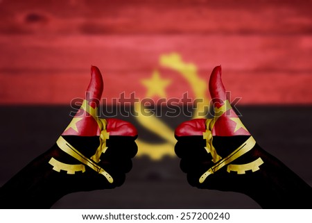 Angola flag painted on female hands thumbs up with blurry wooden background